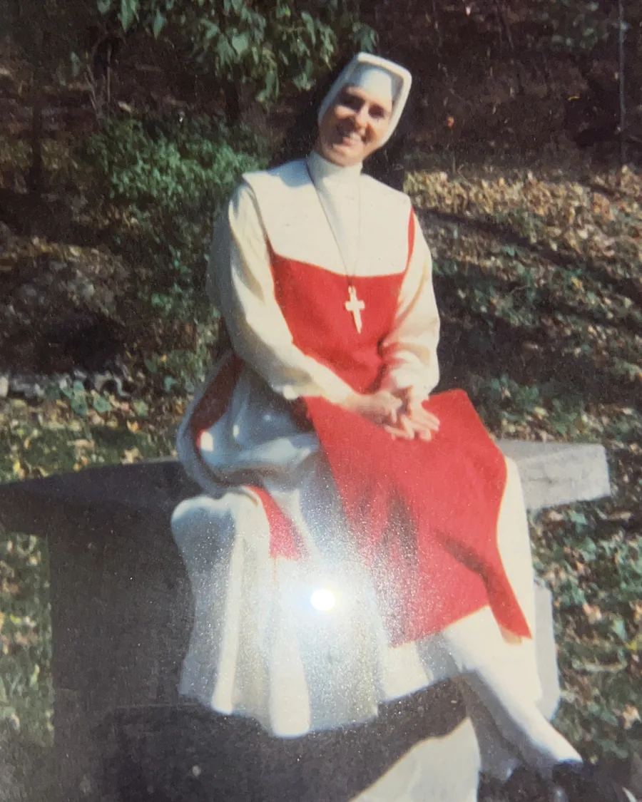 The author&rsquo;s mother as a young nun, seated on a stone bench in the sun, smiling